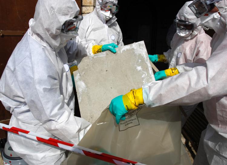 Four people in PPE placing an asbestos sheet into a plastic bag